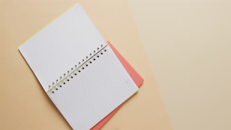 overhead view van open notebook met roze marker met kopieerruimte op beige achtergrond, in slow motion