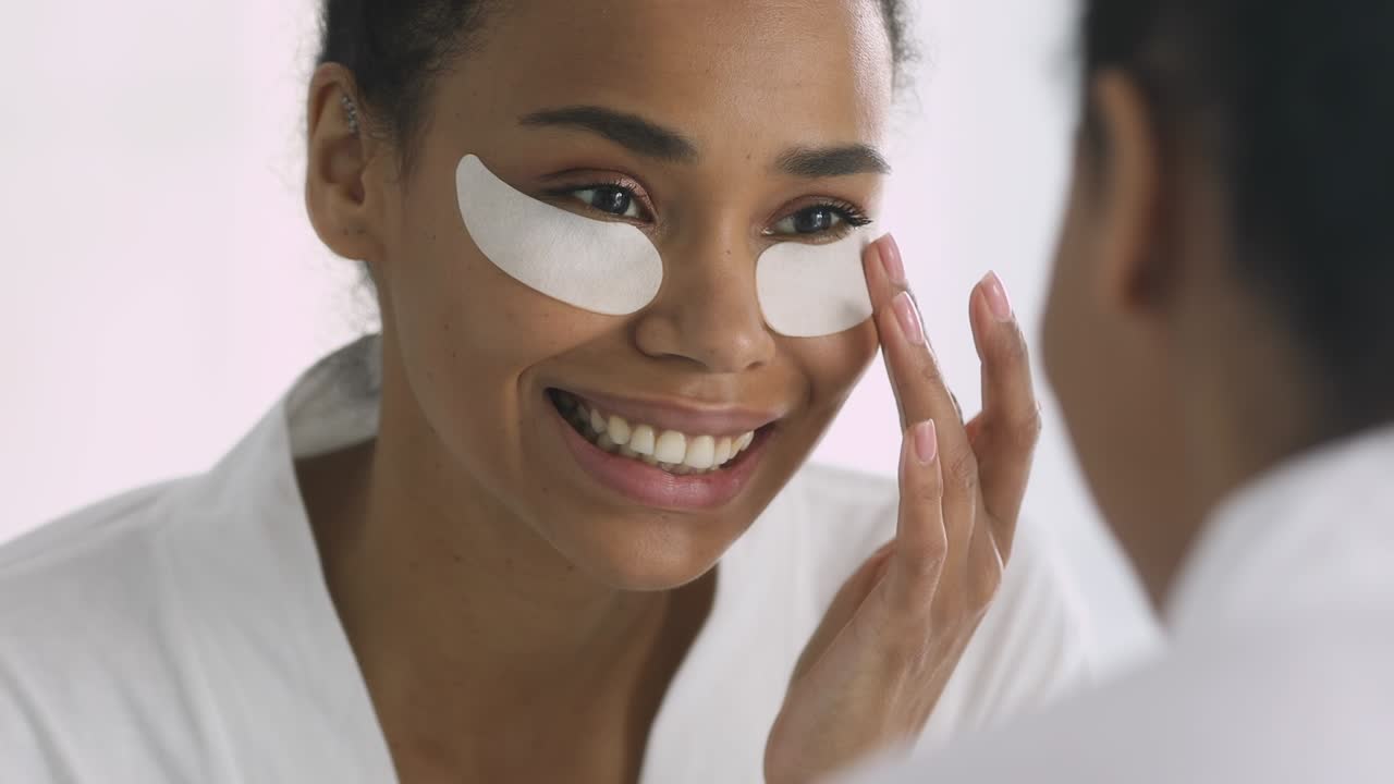Happy african woman with face eye patches looking in mirror