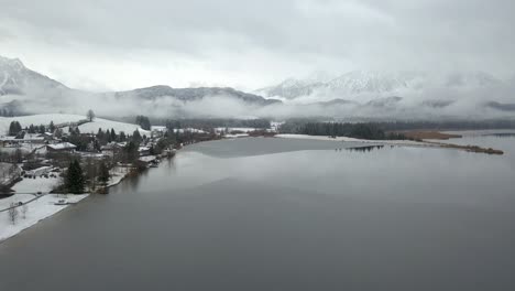 fly over hopfensee lake approaching alps mountains in the winter, bavaria , germany