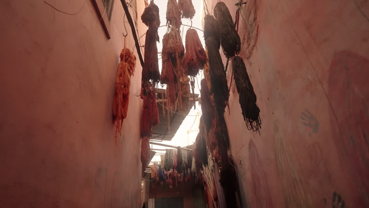 Vibrant dyed yarn skeins hang drying on ropes under the roof of a Moroccan market