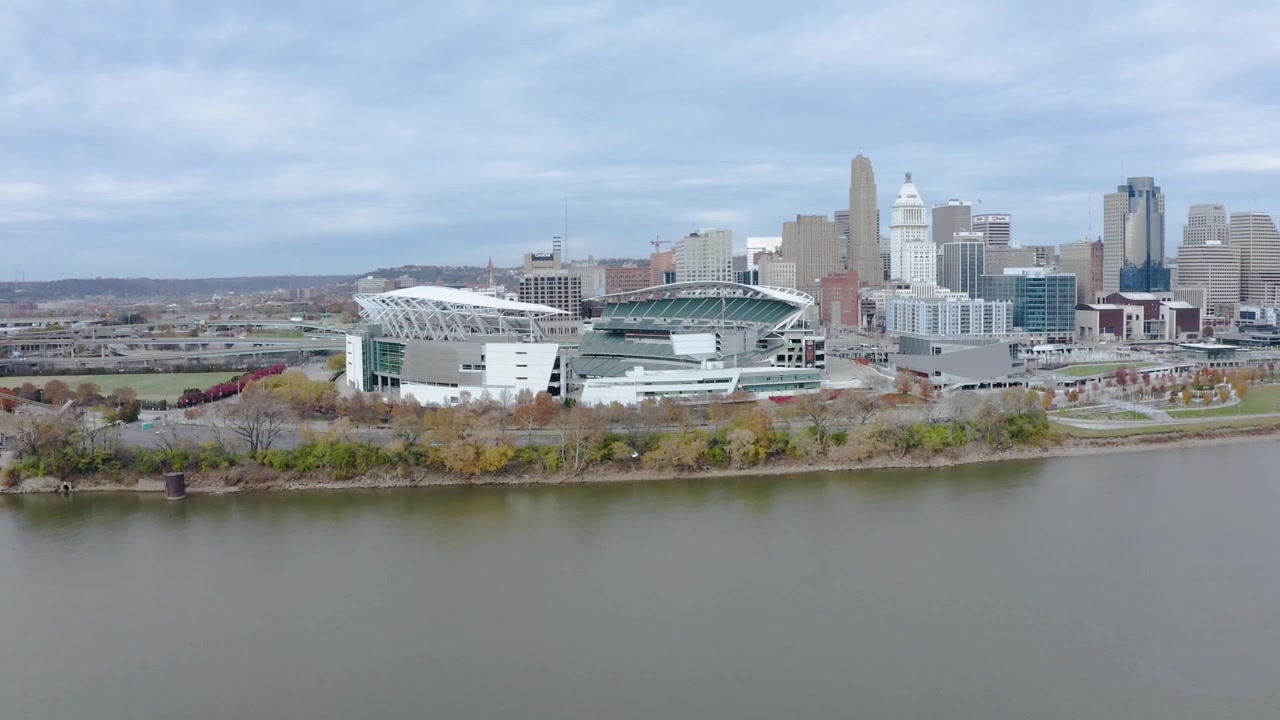 En flygfotograferad panorering av Paul Brown Stadium i Cincinnati, Ohio, över Ohiofloden en mulen dag med livfulla höstfärger i träden och stadssiluett i bakgrunden