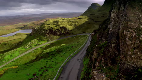 Vista-Aérea-Del-Coche-En-La-Carretera-Del-Campo-En-El-Desierto-De-La-Isla-De-Skye-Escocia-Reino-Unido-Bajo-Acantilados-Escarpados,-Disparo-De-Drones