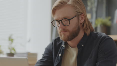 young man working on laptop and looking at camera in office