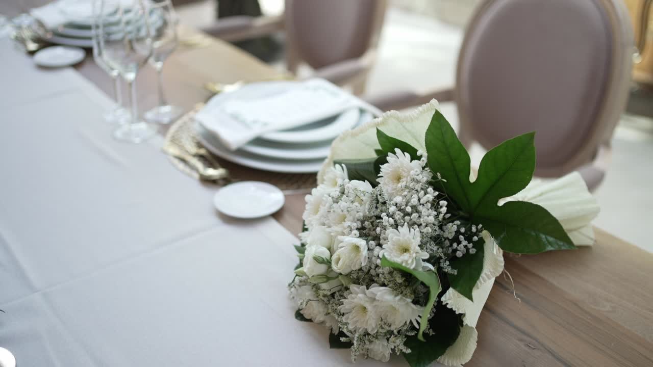 Elegant table arrangement with white floral centerpieces, tall candles, and stacked plates on a soft, neutral-colored tablecloth