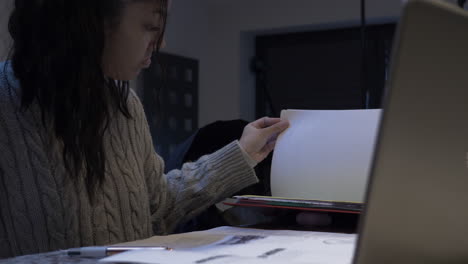 female teenage student taking homework out of folder at home