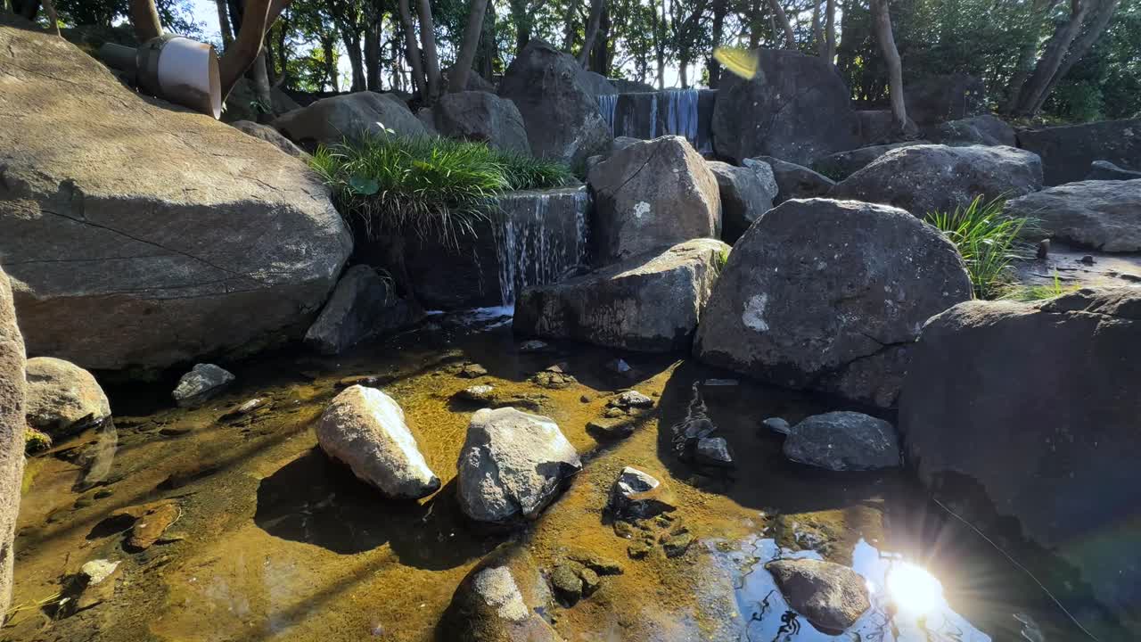 Tranquil stream flowing over rocks in a peaceful Japanese park setting