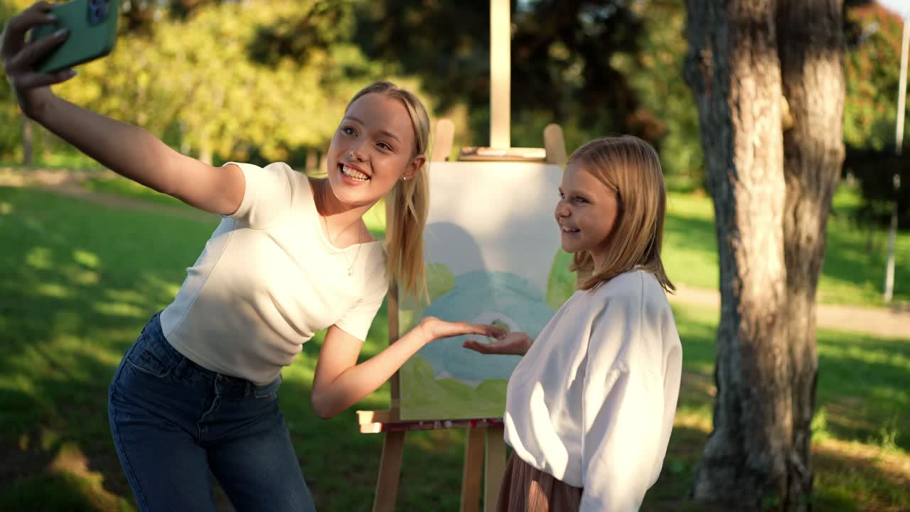 dos chicas tomando una selfie en un parque mientras admiran sus obras de arte