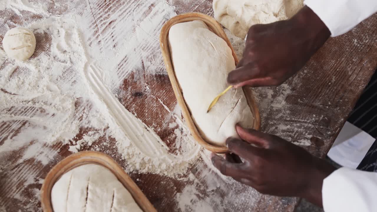 African american male baker working in bakery kitchen, cutting dough for bread in slow motion