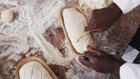 african american male baker working in bakery kitchen, cutting dough for bread in slow motion