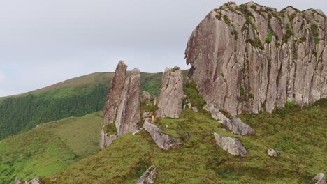 orbit shot of big rock formation man standing in yellow jacket at flores island azores, aerial