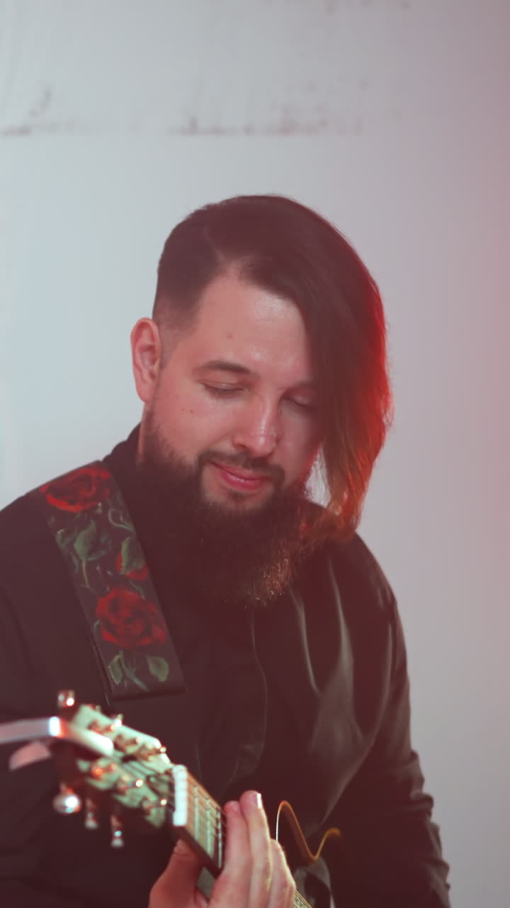 un guitarrista barbudo con un traje negro toca la guitarra contra un fondo blanco. el enfoque está en su expresión enfocada y su habilidad en tocar