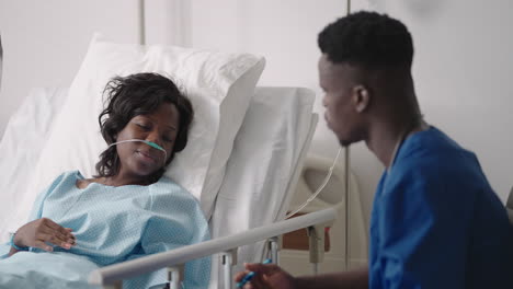 an african male doctor interviews a patient lying in a hospital bed with an oxygen mask. a black woman lying in a hospital bed describes the symptoms to the doctor