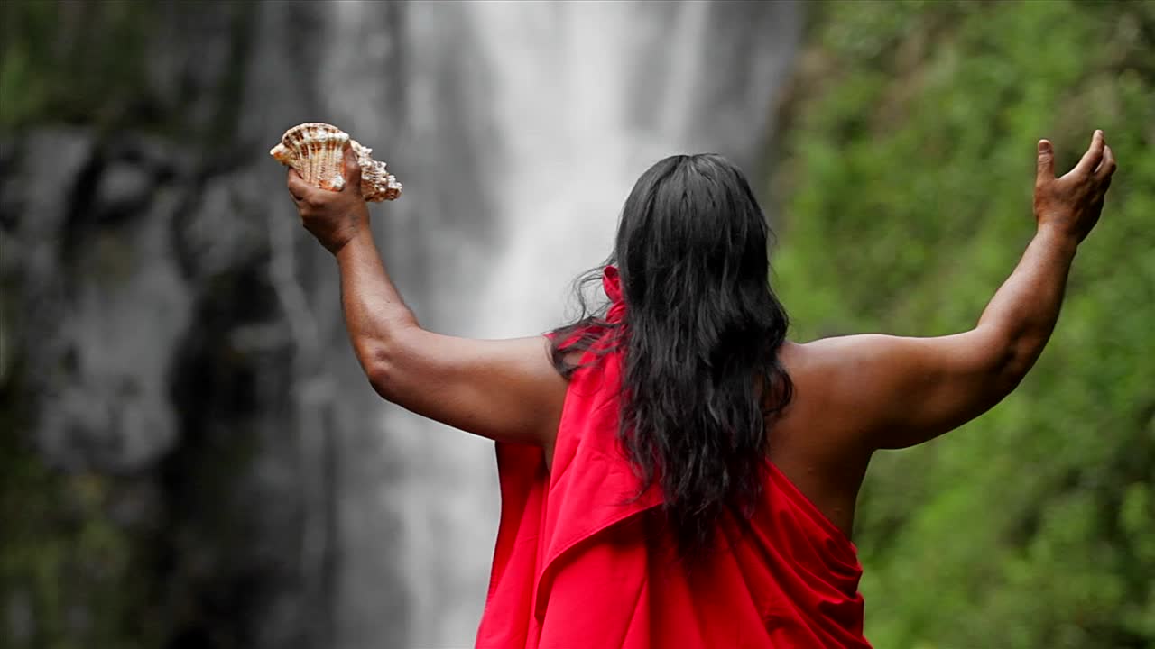 A Hawaii native holds out his hands to bless a waterfall