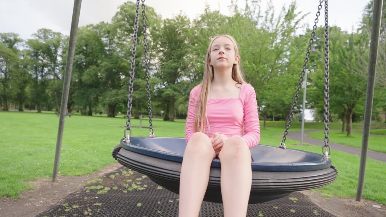 Female child wearing a pink blouse and black skirt sits on kid&rsquo;s swing