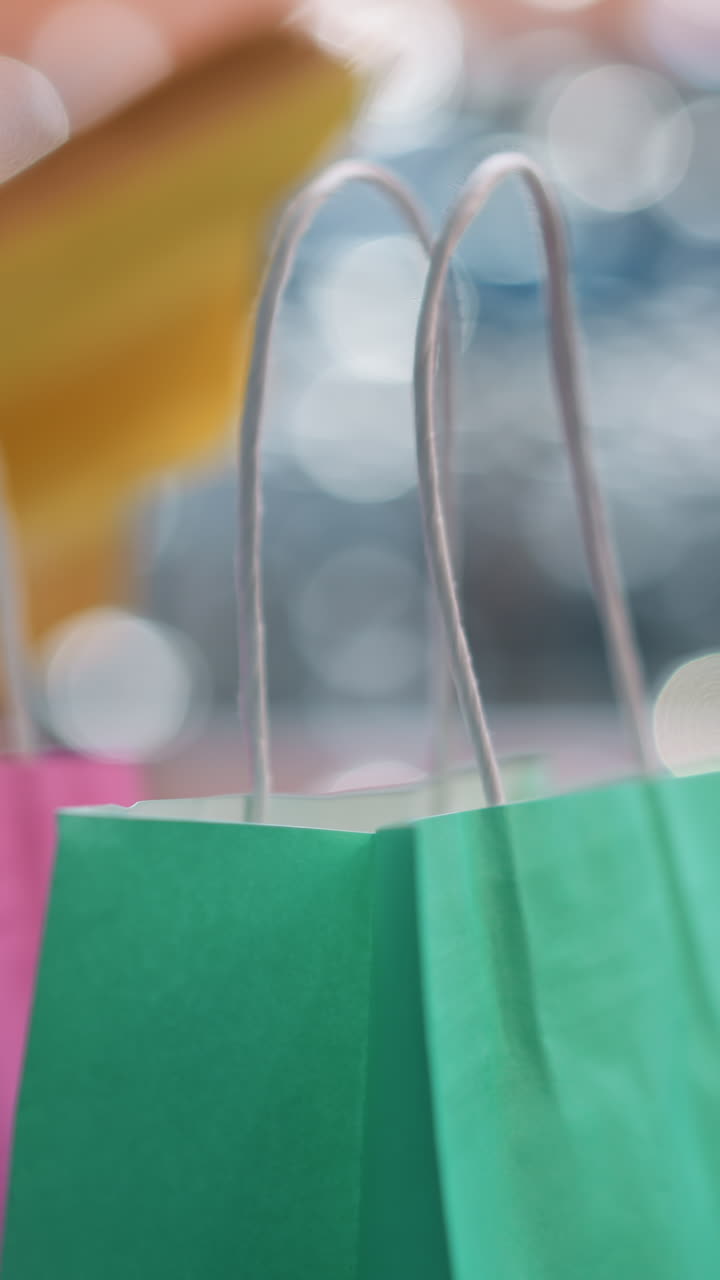 primer plano de bolsas de compras coloridas en primer plano con fondo bokeh borroso, mostrando a una mujer hojeando un libro en un centro comercial