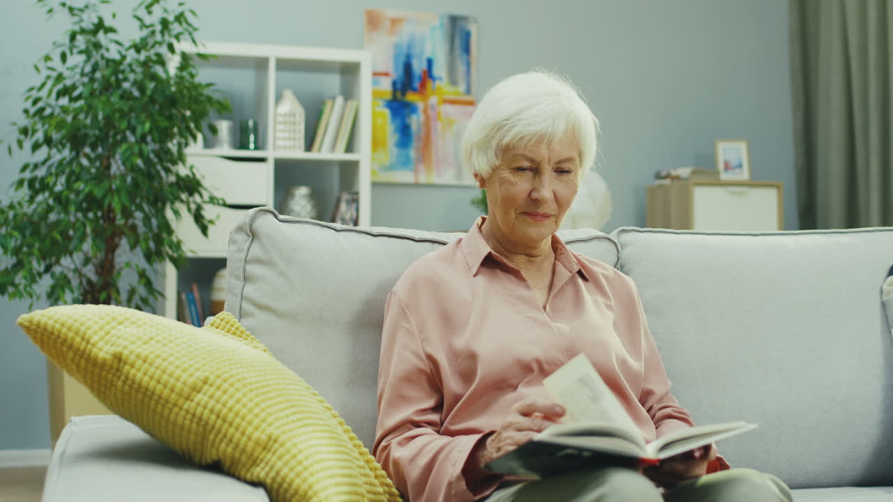 Grandmother Sitting On The Couch At Home While Her Cute Teenager Granddaughter Coming To Her With Copybook From School And Showing Off With Her Good Marks