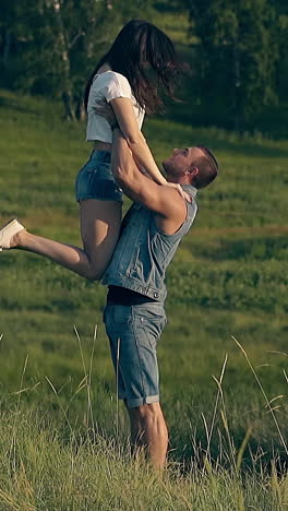 handsome man in denim vest and shorts lifts long haired brunette lady and kisses on summer day slow motion