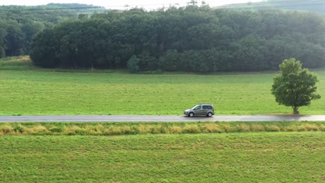 a silver car driving on an asphalt road in front of a forest