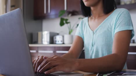 Mixed-race-gender-fluid-person-sitting-at-desk-working-from-home-using-a-laptop