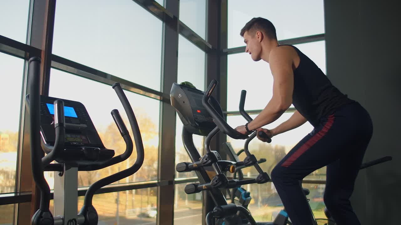 Spor salonunun kardiyo alanında eliptik bisiklette antrenman yapan bir adamın arkadan görünümü