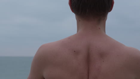 el hombre desnudo medita, cerca del mar tranquilo, sus músculos se flexionan mientras inhala y exhala profundamente antes de inclinarse al final