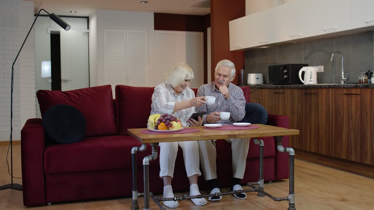 Senior old couple grandparents talking and using digital tablet computer at home. Internet shopping