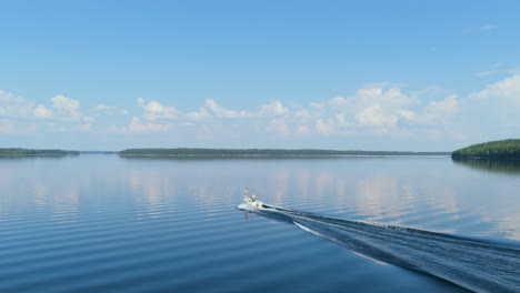 drone tracking a boat driving on reflecting lake saimaa, summer day in finland