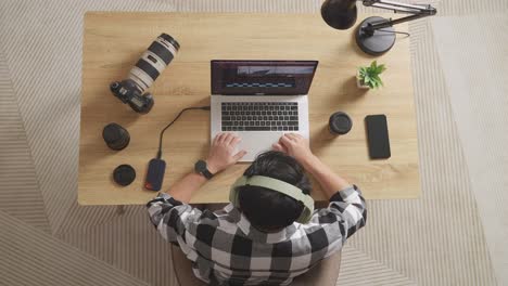 top view of a male editor with headphone celebrating succeed using a laptop next to the camera editing the video in the workspace at home