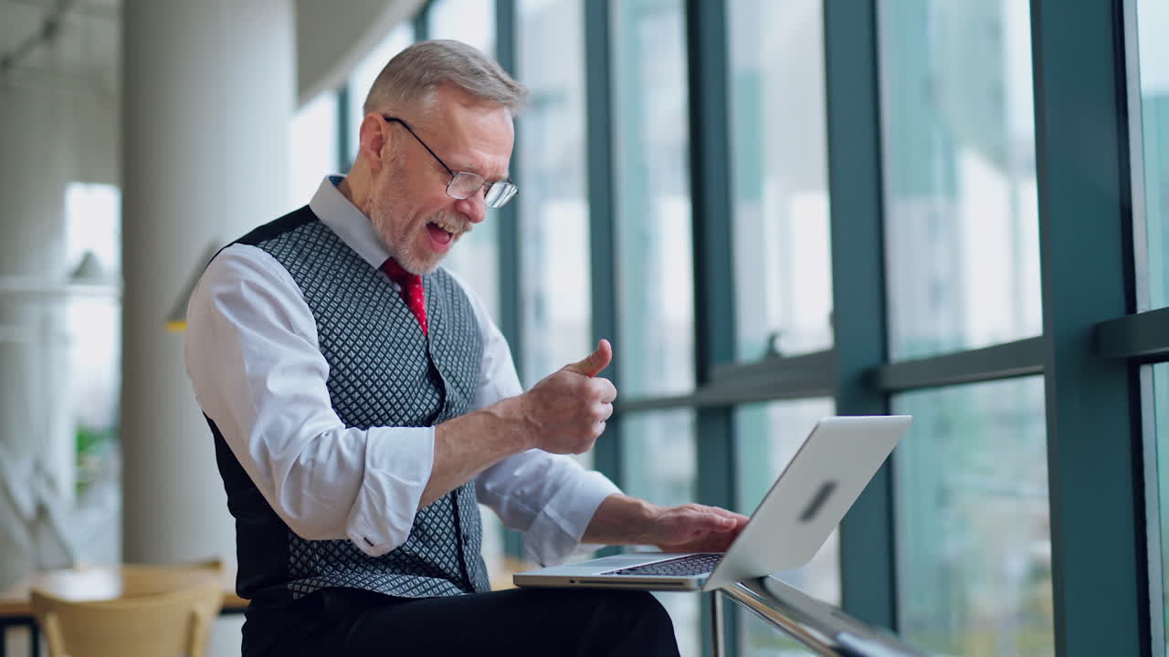 Freelance senior man working on a laptop. Mature man becomes happy after doing a successful job on a computer at home.