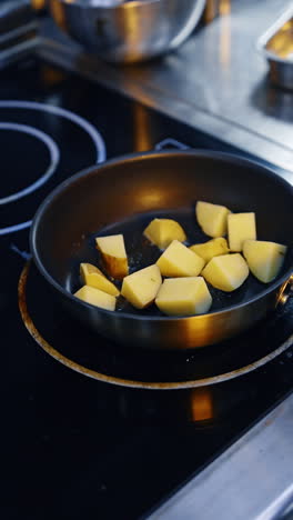 cubes of the unpeeled potatoes are put on the preheated frying pan. cooking vegetables. close up. vertical video.