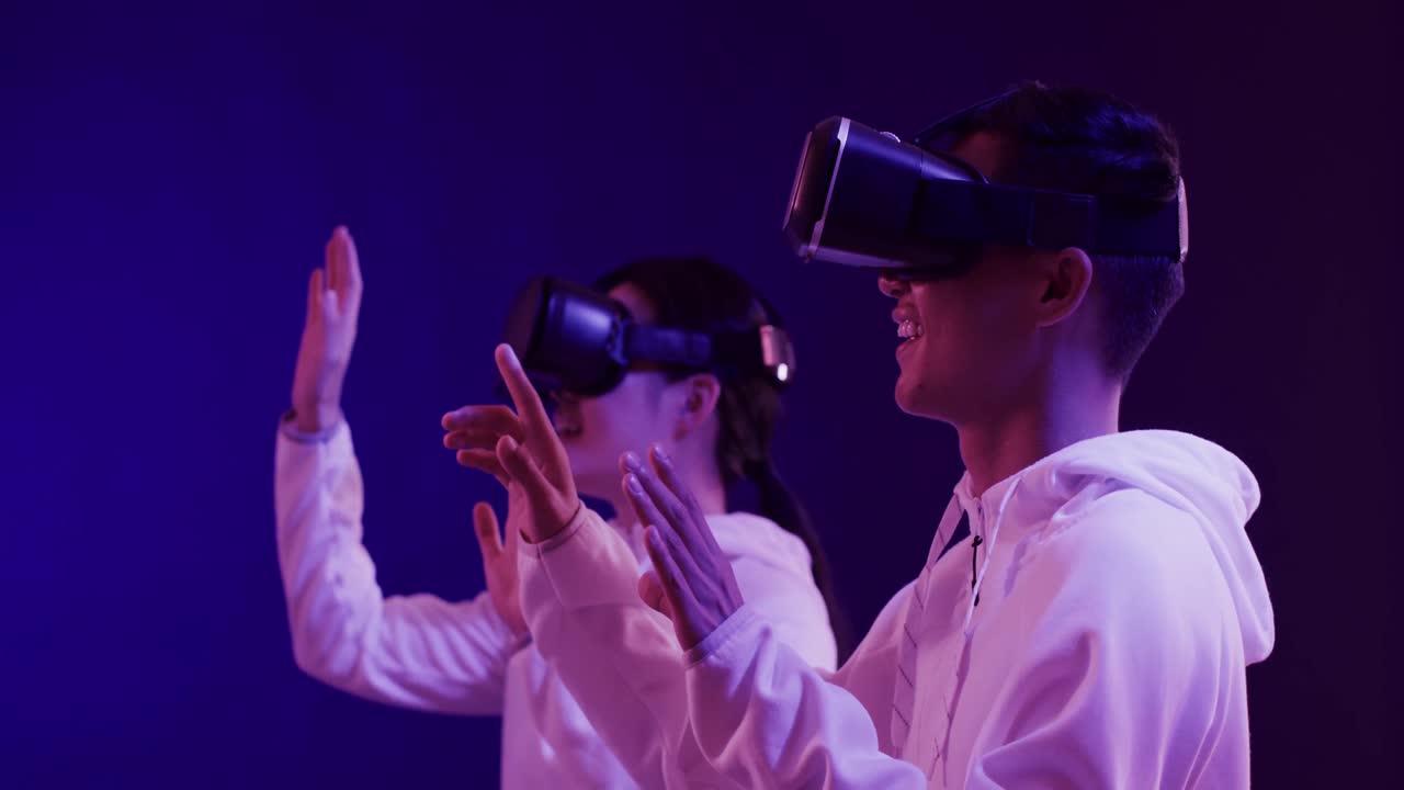Asian man and woman using vr headsets, touching virtual screen on blue background, slow motion