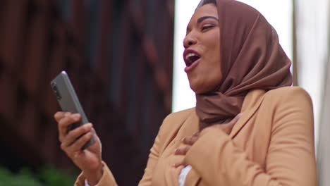 Muslim-Businesswoman-Wearing-Hijab-Standing-Outside-Modern-Office-Getting-Good-News-About-Job-Offer-Or-Promotion-On-Mobile-Phone-4