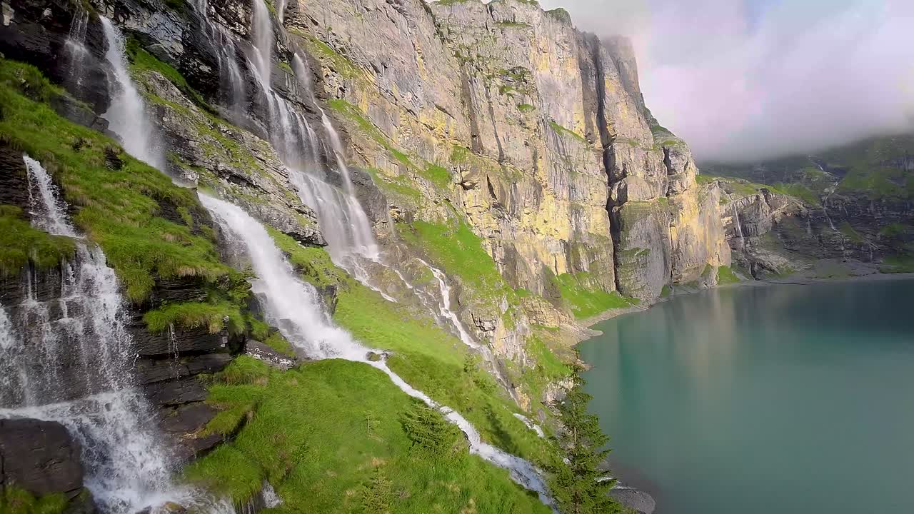 Volo con drone vicino a una grande e bellissima cascata in un paesaggio montano, sopra un lago blu - Lago di Oeschinen, Svizzera