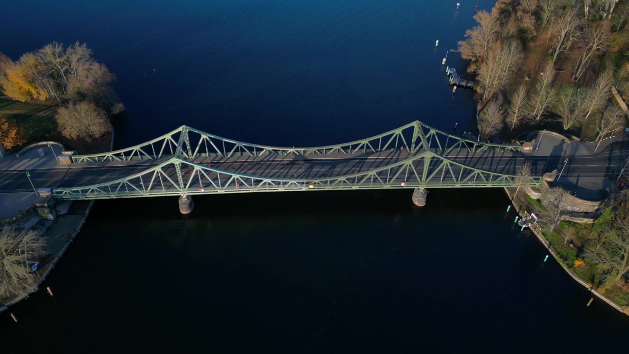 Glienicken silta Havel-joen yli, autojen ajaessa sitä pitkin värikkään syksyisen auringonlaskun aikaan. Upea ilmakuva dronella, kamera osoittaa alaspäin.