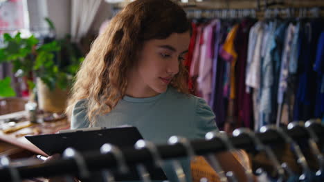 Female-Owner-Or-Worker-In-Fashion-Clothing-Store-Checking-Stock-With-Clipboard