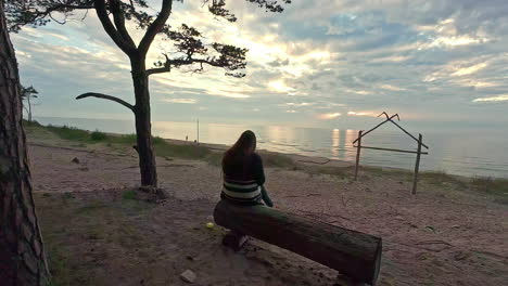 lonely woman sitting on wooden bench on sea coastline, back moving shot