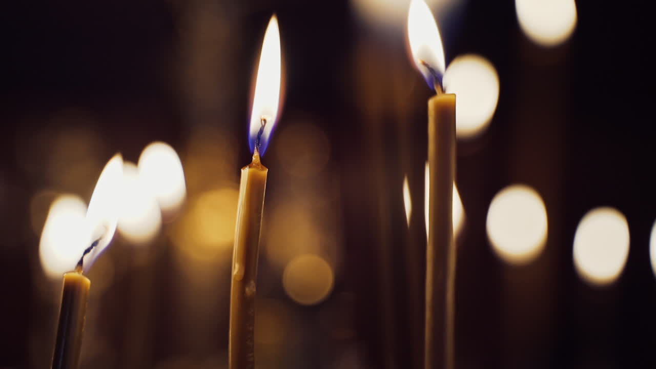 Candles flame brightly in the church. Burning candles on the blurred background with light spots. Close-up