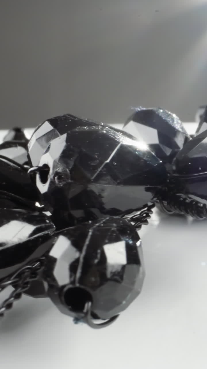Lustrous black gemstone necklace on a white surface with a radiant light flare
