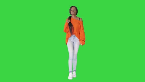 smiling african american woman dressed in bright sweater and jeans walking touching her hair on a green screen, chroma key