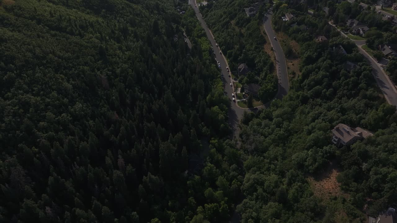 A wide aerial drone dolly in tilting up shot from Bountiful Canyon showing a road, forest, valley homes, cityscape, mountains, and the Great Salt Lake on a clear summer day