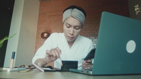 woman applying makeup while working on laptop