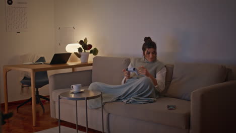 focused woman playing video game at evening home. positive lady checking phone