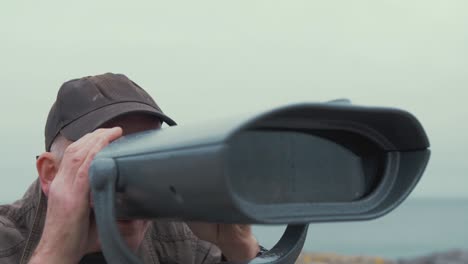 elderly man looks through binoculars sight seeing viewing at scenic landscape real time