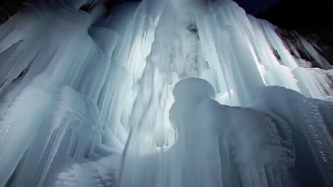 witness the beauty of frozen ice formations hanging against a serene mountain backdrop during the winter season. experience the intricate textures and colors of nature's art.