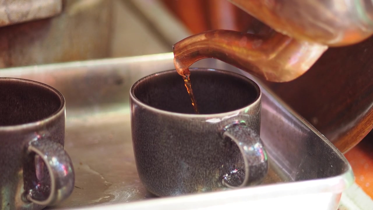Despejando Chá Quente de uma Chaleira de Cobre em uma Xícara de Cerâmica