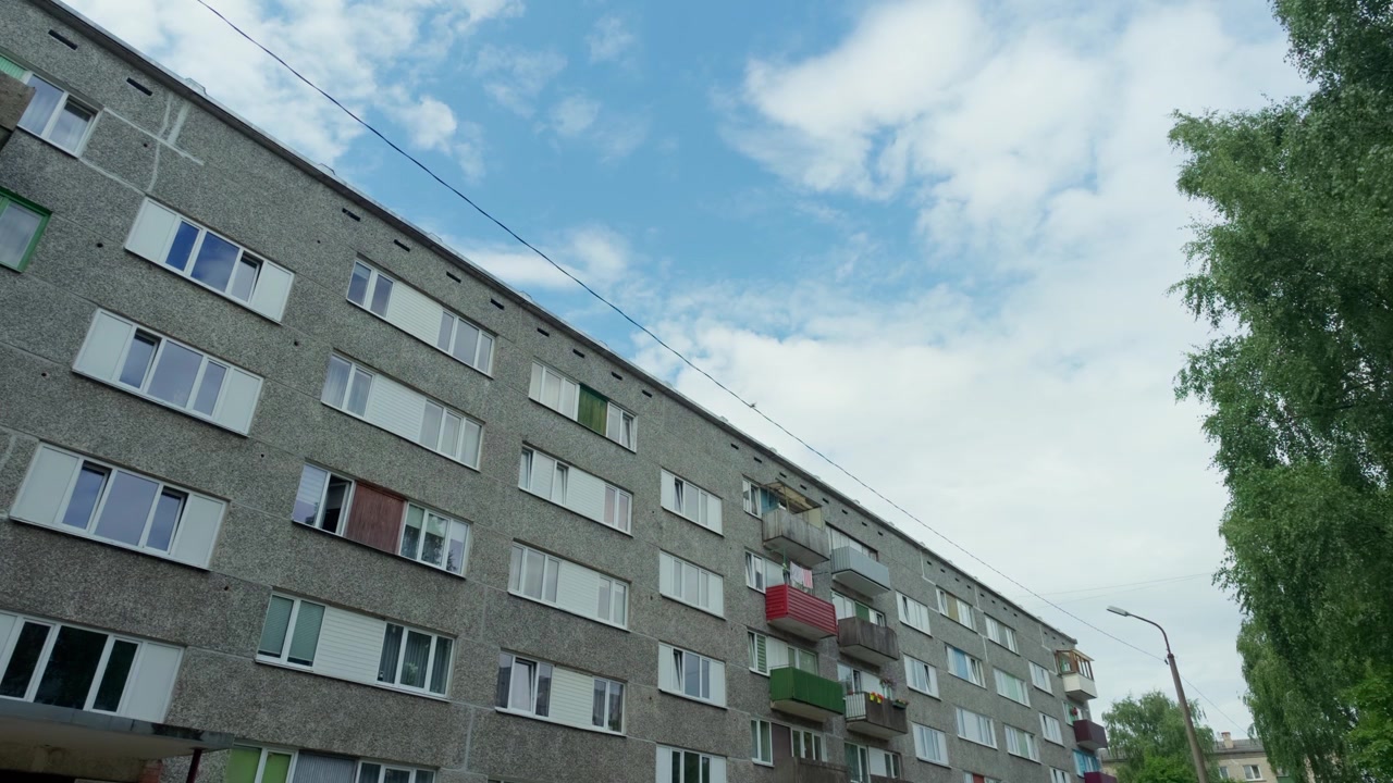 Untersicht der Betonfassade eines Wohnblocks aus der Sowjetzeit unter bewölktem Sommerhimmel in Daugavpils, Lettland, Weitwinkel-Außenaufnahme.
