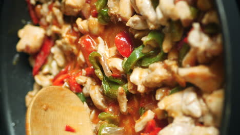 wooden spoon stirring chicken, vegetable fajita mix in skillet vertical close up