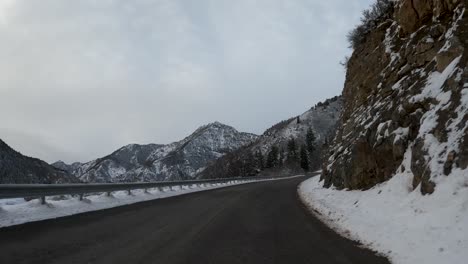 Winter-POV-Aufnahme-Eines-Autos,-Das-Verschneite,-Felsige-Bergstraße-Fährt