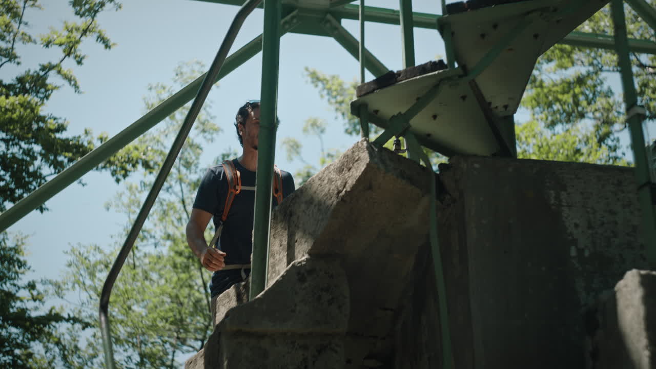 hombre acercándose a una escalera de caracol y comenzando a caminar sobre ella con una mochila naranja para llegar a la cima de una torre de vigilancia