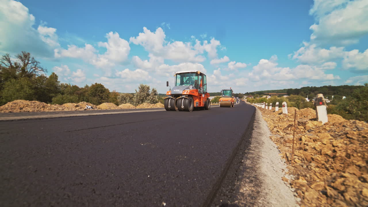 Process of pressing fresh asphalt on the road in a bright sunny day. Two new compactors working on the new road leveling up hot bitumen in summer.